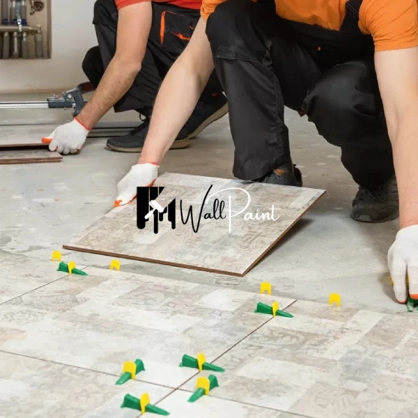 Two workers in orange shirts and gloves are tile fixing a floor using spacers for even grout lines.