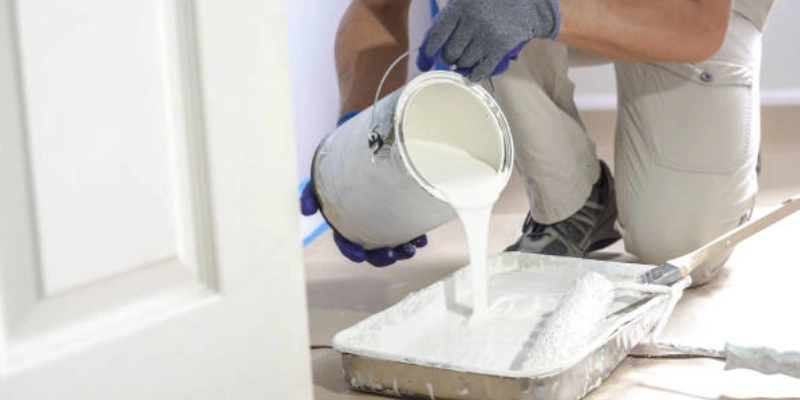 Painter pouring white paint into tray for wall painting Dubai.